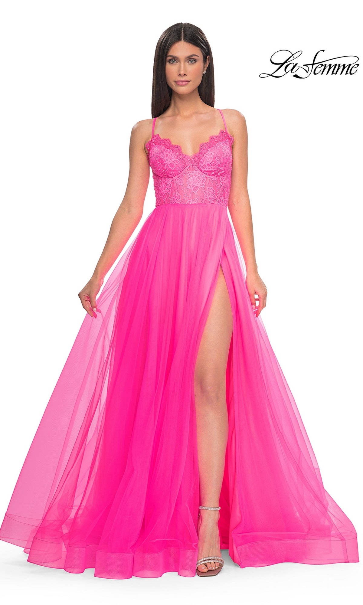 A woman poses against a white background in the La Femme Lace-Bodice Long A-Line Prom Dress 32306, featuring bright pink sheer fabric, a lace bodice, floor-length skirt, and thigh-high slit.